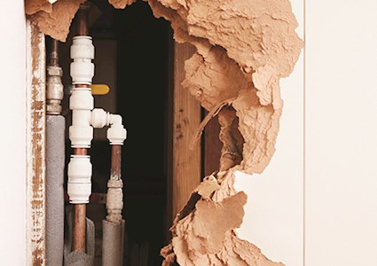 Damaged wall exposing burst water pipes