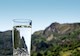 A clear glass of water with blue sky and green mountain landscape background 