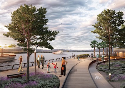 Rendering shows people walking along a wooden boardwalk. To the left is a body of water, and there are yachts in the water. To the right of the boardwalk are trees and a pavilion.