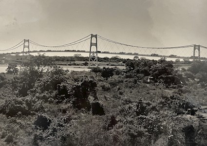 Sepia-toned photo shows a cable-stayed bridge that spans a body of water. Cars are on the bridge. 