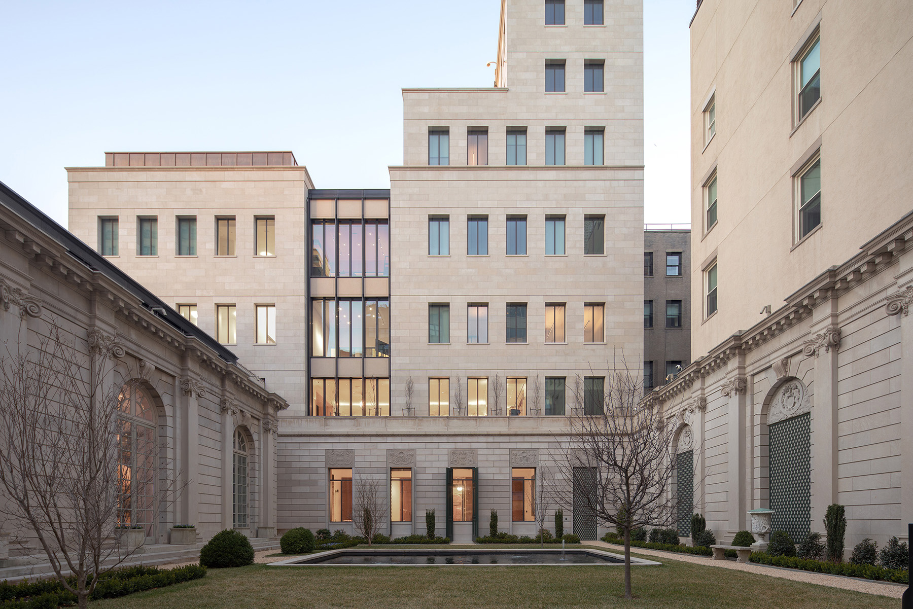 Image shows several multistory stone buildings. The building in the center has a rectangular pool in front of it. 