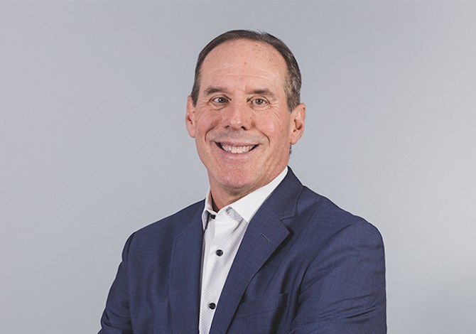 Studio headshot of an adult professional wearing a navy blazer and white shirt, facing slightly to the side against a light gray background.