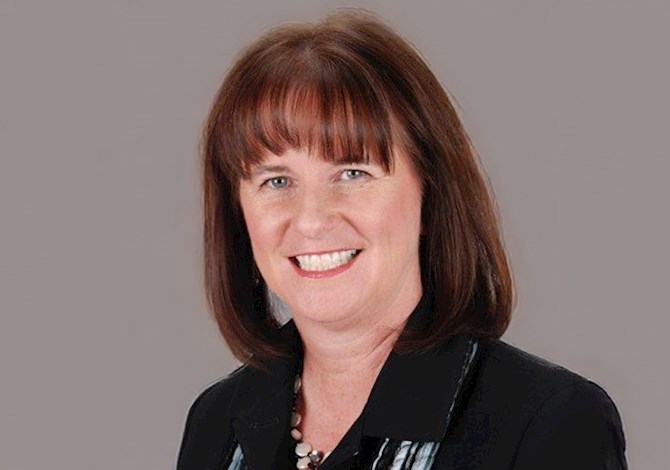 Studio headshot of an adult professional wearing a dark blazer and patterned top, photographed against a light neutral background.