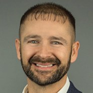 Man in jacket and shirt smiles at the camera.